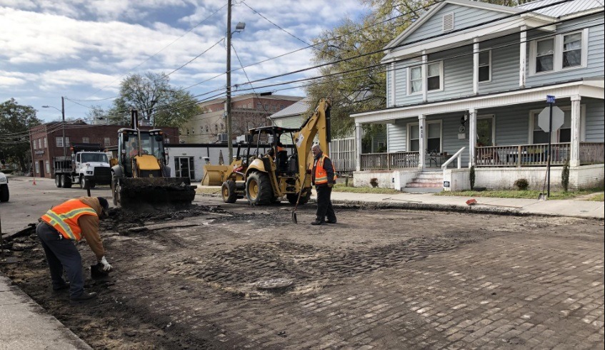 Workers removing asphalt exposing old brick pavers